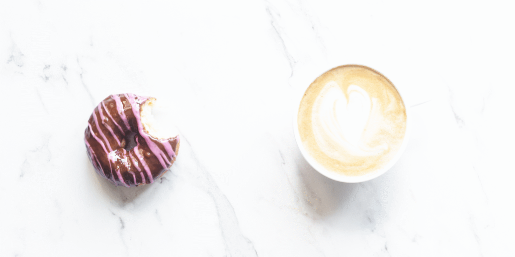 A bitten chocolate donut next to a latte with heart-shaped foam art