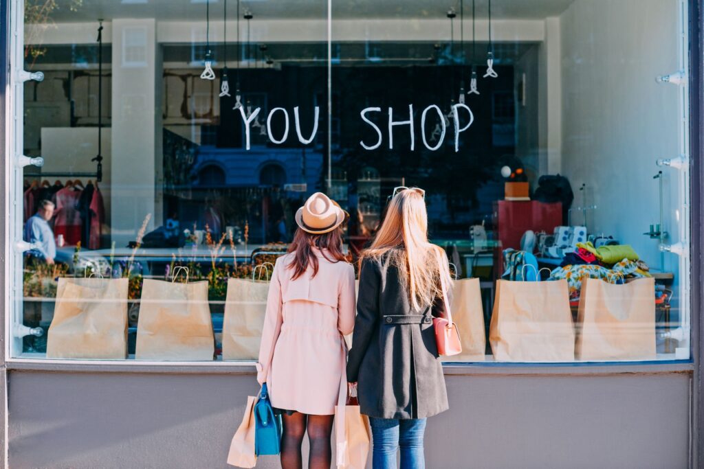 Two women carrying shopping bags looking into a storefront window
