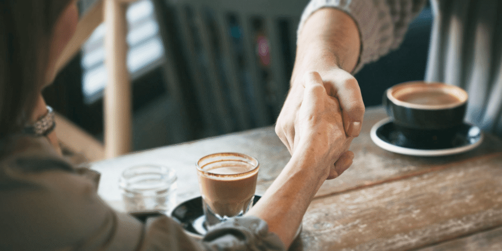Two people shaking hands over cups of coffee at a wooden table