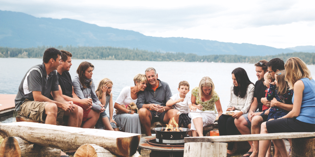 A large family gathered around a campfire by a lake