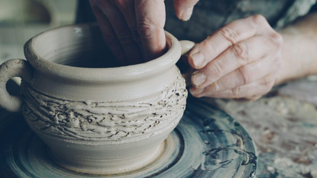 A potter shapes wet clay into a bowl on a pottery wheel