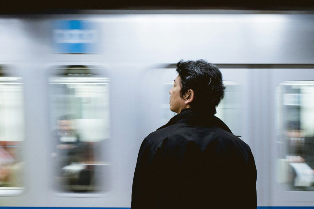 A man waits on a subway platform as a train blurs past